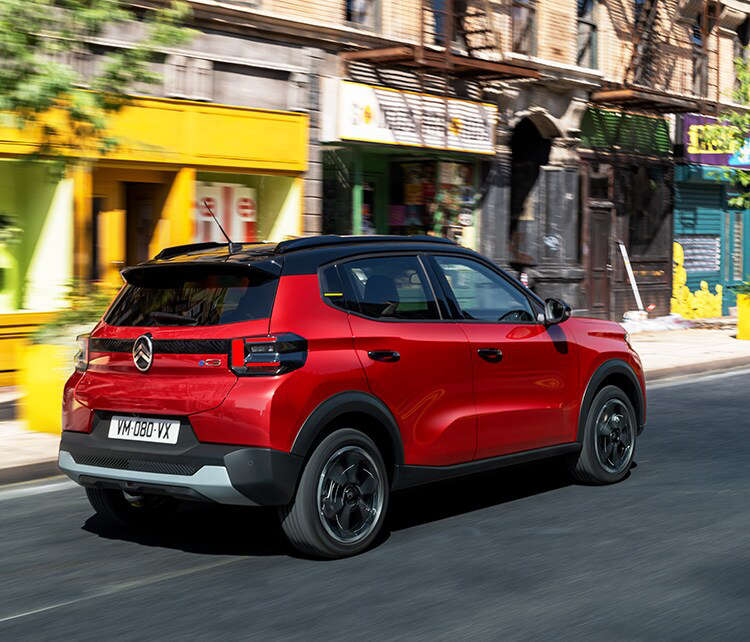 Citroën ë-C3 червоного кольору їде по вулиці, вигляд ззаду з правого боку